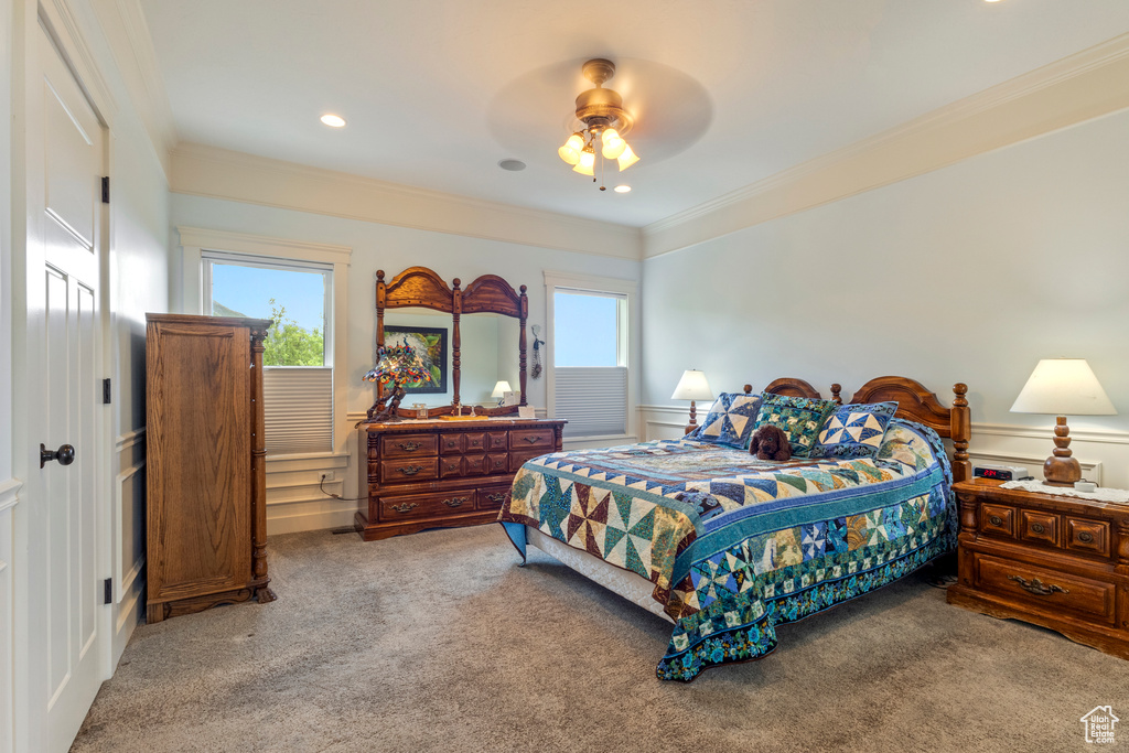 Bedroom featuring carpet floors, a decorative wall, ornamental molding, wainscoting, and a ceiling fan
