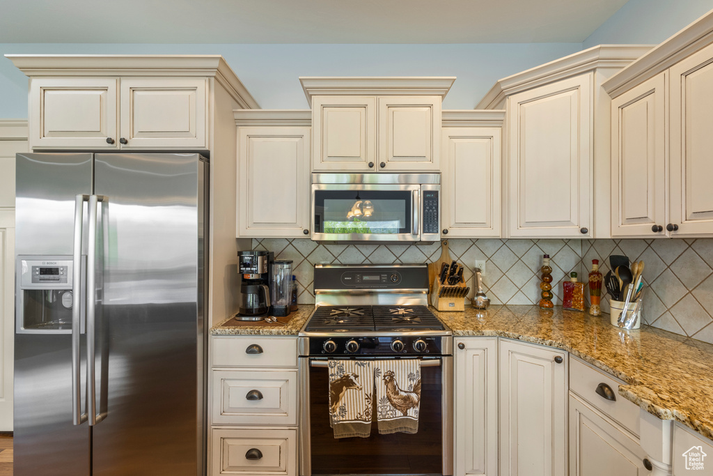 Kitchen with stainless steel appliances, cream cabinetry, and light stone countertops