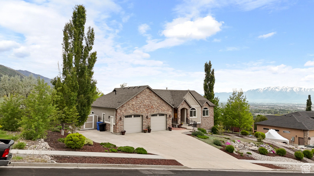 French country inspired facade with a garage, stone siding, concrete driveway, and a mountain view