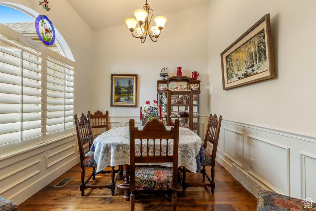 Dining space featuring a chandelier, a decorative wall, a wainscoted wall, wood finished floors, and vaulted ceiling