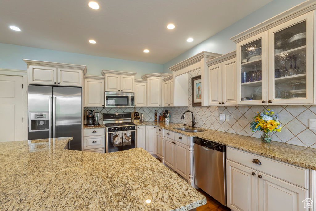 Kitchen with stainless steel appliances, a sink, cream cabinets, and recessed lighting