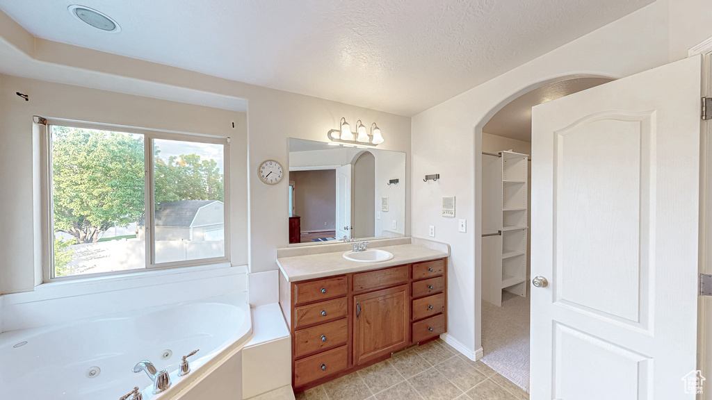 Bathroom featuring vanity, a whirlpool tub, a textured ceiling, a walk in closet, and tile patterned flooring