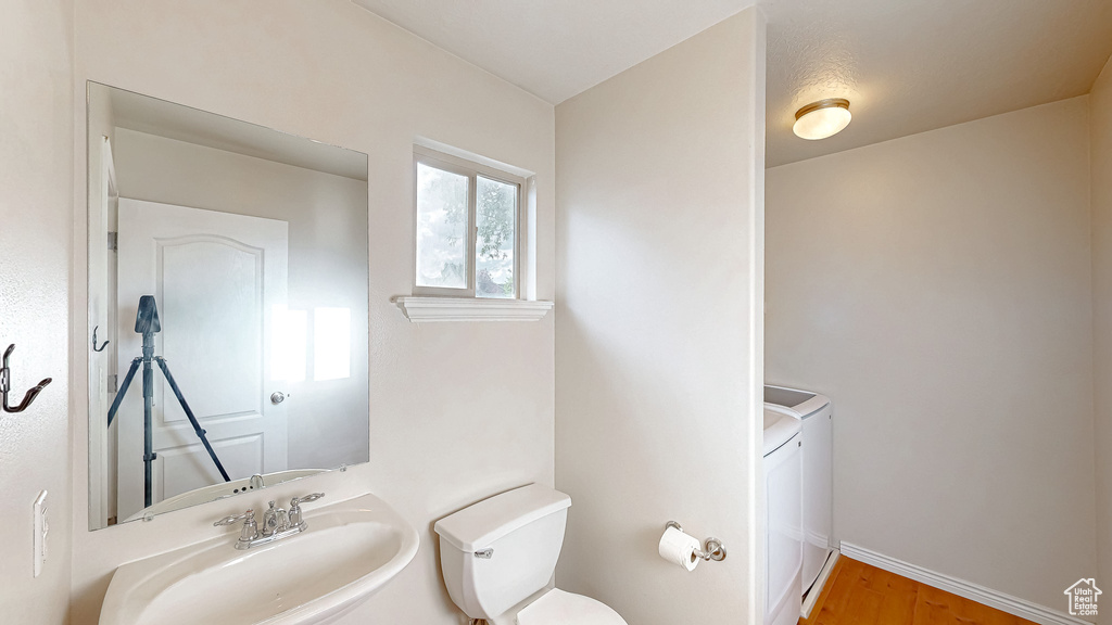 Half bathroom featuring toilet, a sink, washing machine and dryer, wood finished floors, and baseboards
