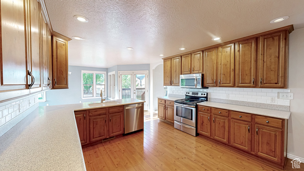 Kitchen with appliances with stainless steel finishes, a sink, light wood-style flooring, light countertops, and recessed lighting