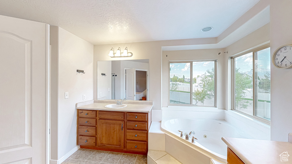 Full bathroom with vanity, plenty of natural light, a tub with jets, tile patterned floors, and a textured ceiling