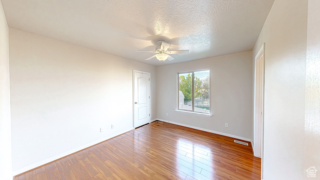 Empty room with wood finished floors, a ceiling fan, baseboards, and a textured ceiling