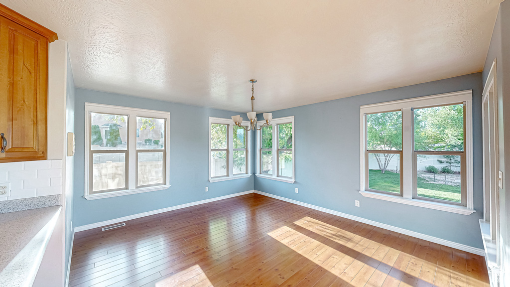 Unfurnished dining area featuring a chandelier, hardwood / wood-style floors, and healthy amount of natural light