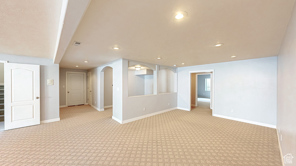 Empty room featuring stairway, baseboards, recessed lighting, light colored carpet, and arched walkways