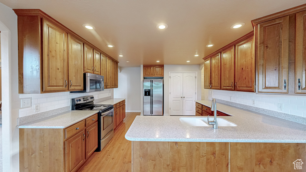 Kitchen with appliances with stainless steel finishes, a sink, a peninsula, recessed lighting, and backsplash