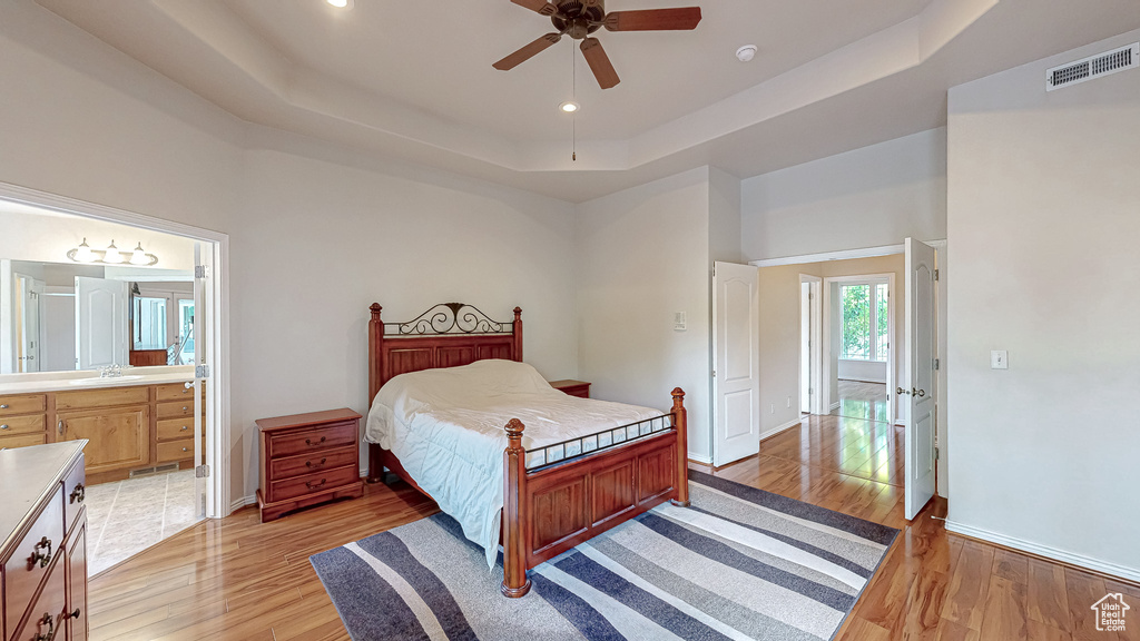 Bedroom with a tray ceiling, a sink, light wood-type flooring, baseboards, and recessed lighting