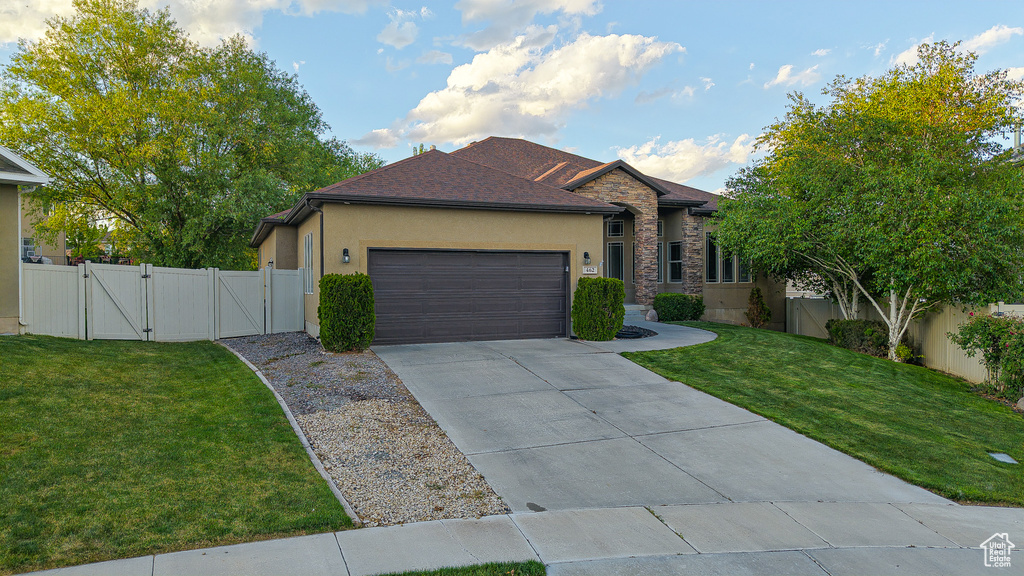 Ranch-style home with a gate, stucco siding, an attached garage, driveway, and stone siding