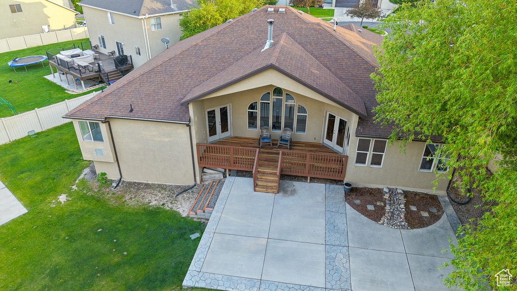 Rear view of property featuring roof with shingles, stucco siding, a deck, a patio, and a trampoline