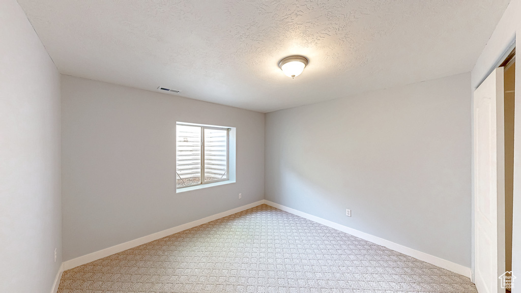 Spare room with light carpet, a textured ceiling, and baseboards
