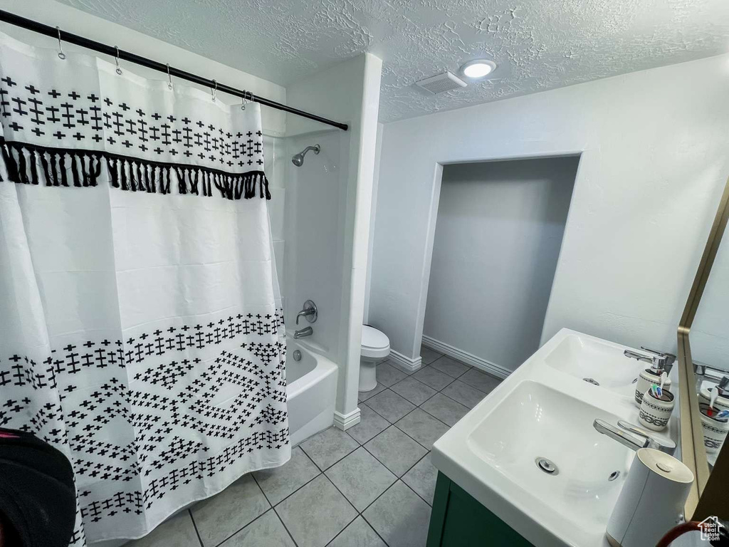 Full bath featuring a textured ceiling, tile patterned floors, shower / bath combo with shower curtain, toilet, and vanity