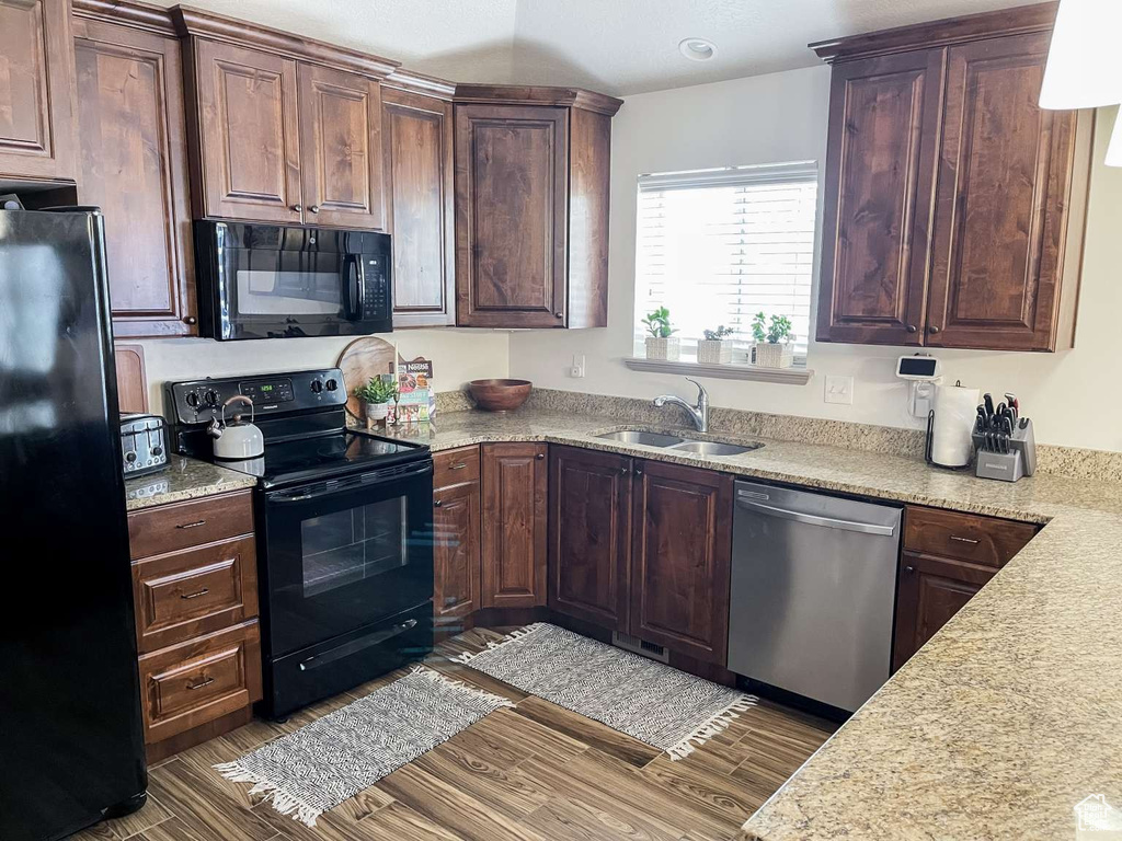 Kitchen with black appliances, a sink, wood finished floors, and dark brown cabinets