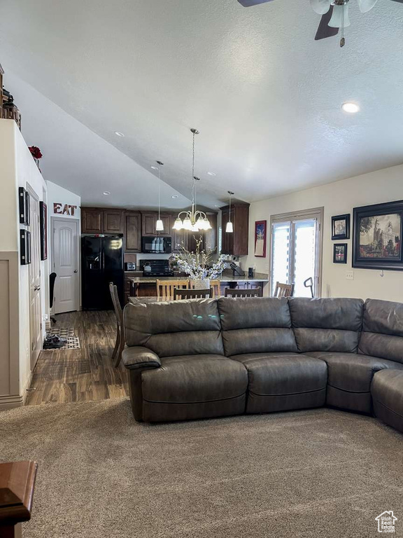 Living area featuring ceiling fan, a chandelier, vaulted ceiling, dark colored carpet, and dark wood-style flooring