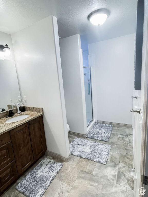 Full bath with a textured ceiling, a stall shower, vanity, toilet, and baseboards