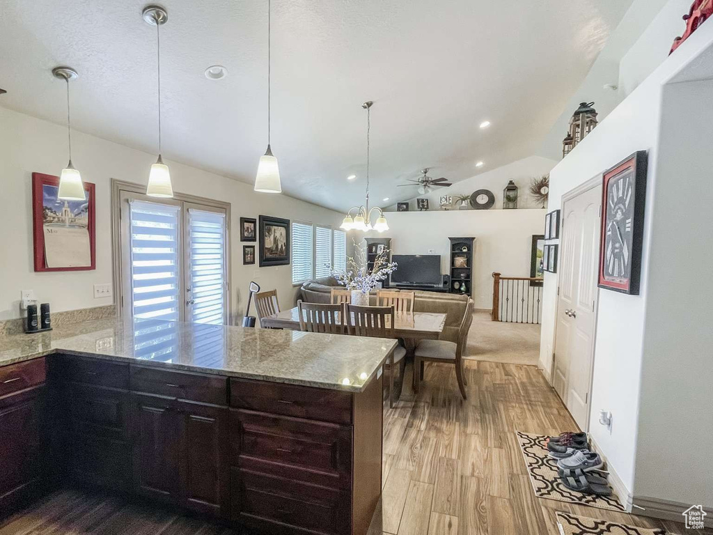 Kitchen featuring a peninsula, wood finished floors, light stone countertops, lofted ceiling, and a ceiling fan