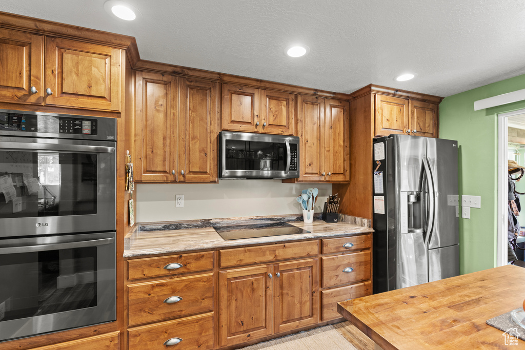 Kitchen featuring appliances with stainless steel finishes, brown cabinetry, butcher block countertops, and recessed lighting