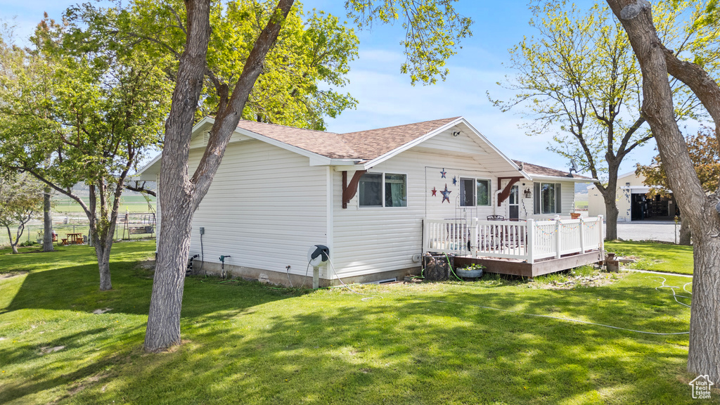 Back of property featuring a deck, a yard, and a shingled roof