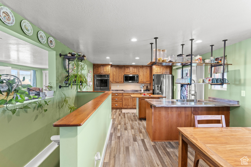 Kitchen featuring stainless steel appliances, a peninsula, light wood finished floors, brown cabinets, and recessed lighting