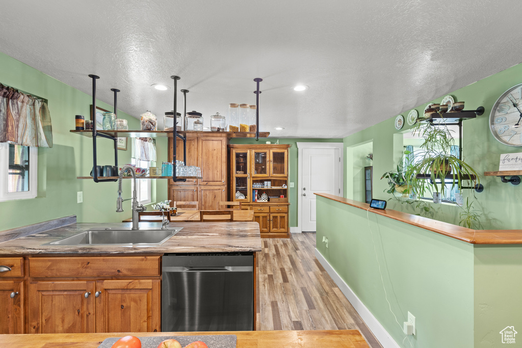 Kitchen featuring a sink, stainless steel dishwasher, light wood-style floors, a textured ceiling, and brown cabinetry