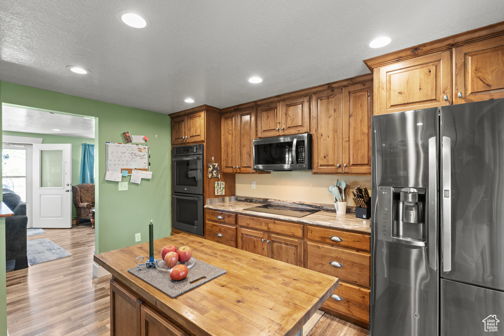 Kitchen with black appliances, light wood-style flooring, brown cabinetry, recessed lighting, and wood counters