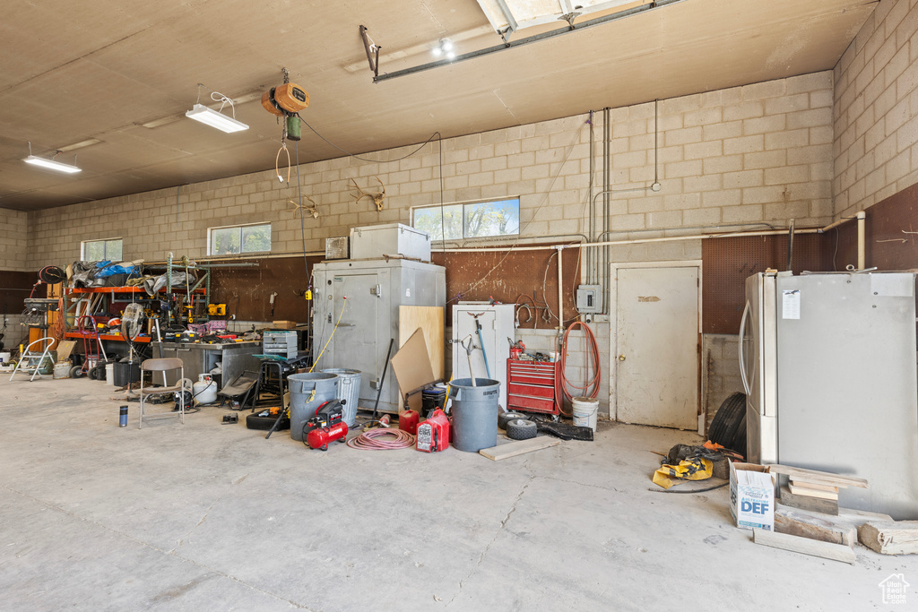 Garage featuring freestanding refrigerator, concrete block wall, and a workshop area