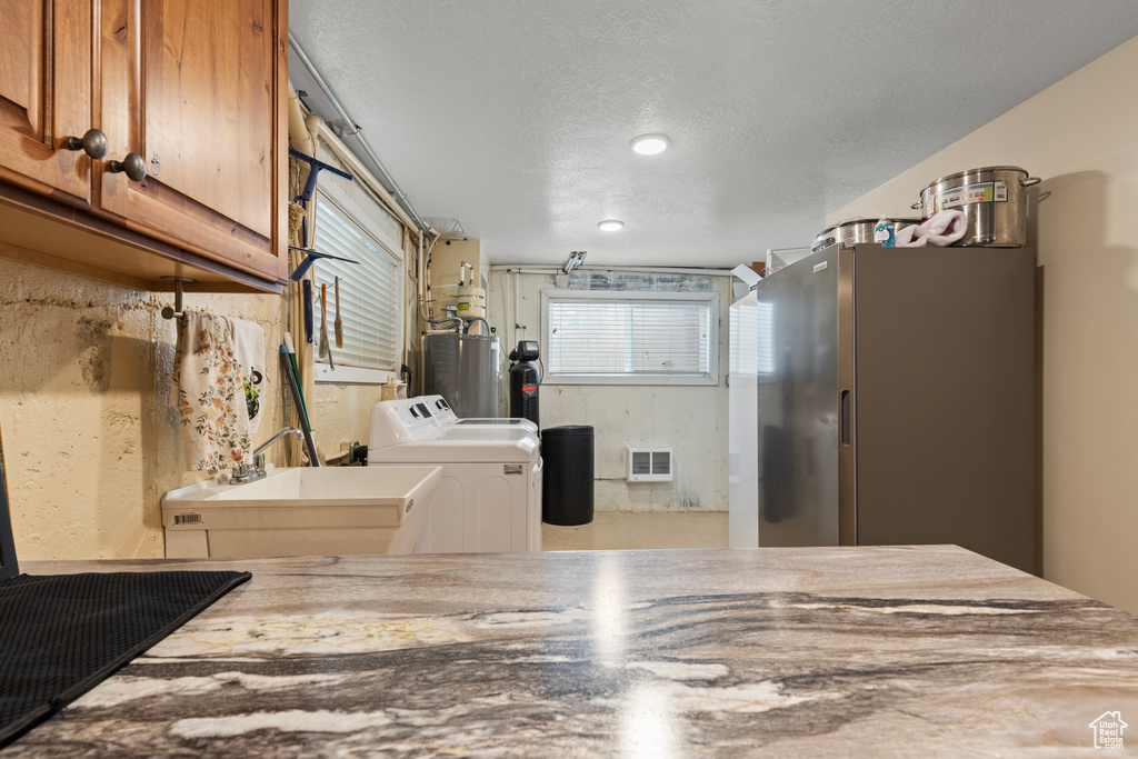 Kitchen featuring separate washer and dryer, gas water heater, brown cabinetry, freestanding refrigerator, and a textured ceiling