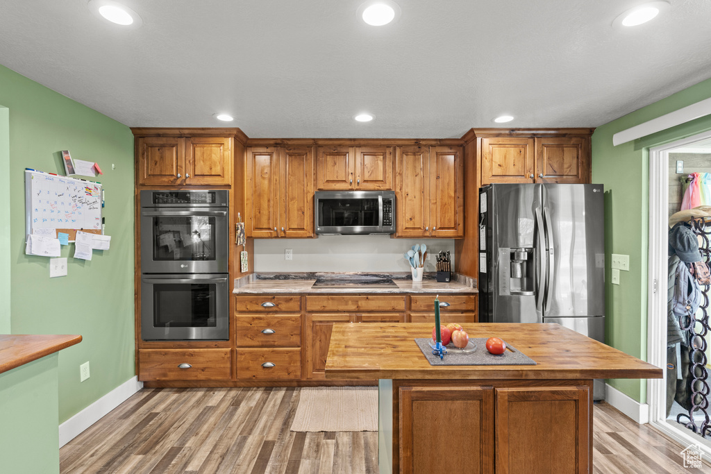 Kitchen featuring appliances with stainless steel finishes, light wood-type flooring, wood counters, recessed lighting, and brown cabinets