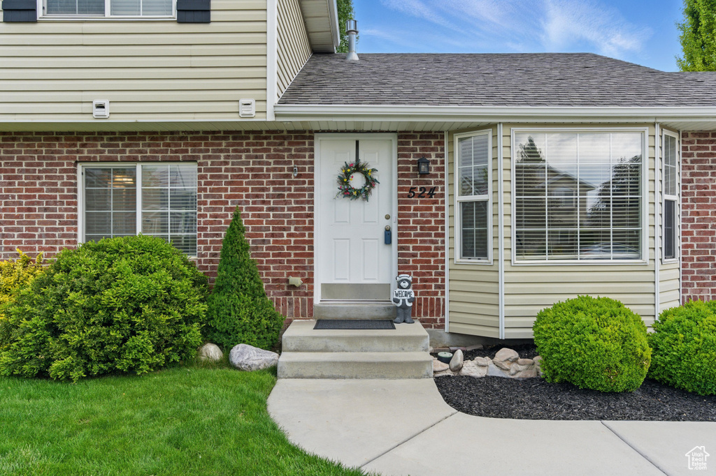 Property entrance featuring brick siding and a shingled roof