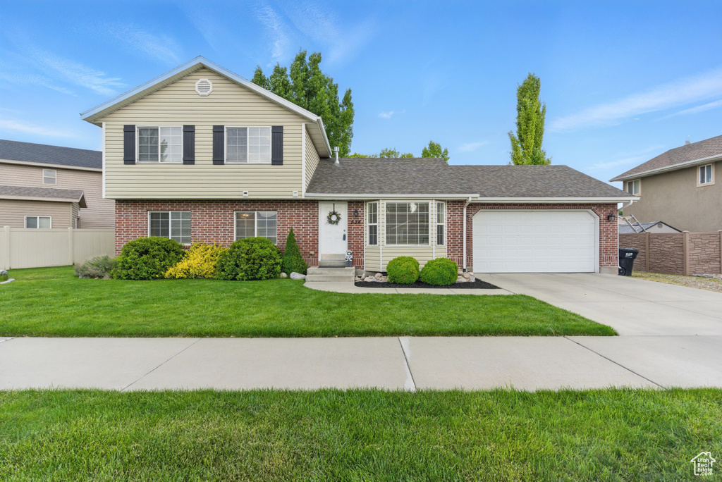 Tri-level home with brick siding, a garage, concrete driveway, and roof with shingles