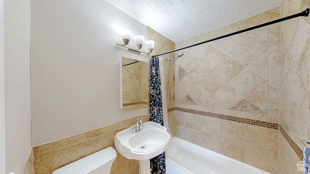 Bathroom with a textured ceiling, a chandelier, shower / bathtub combination with curtain, toilet, and a sink