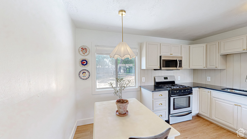 Kitchen with stainless steel appliances, a sink, light wood-style floors, dark countertops, and white cabinetry