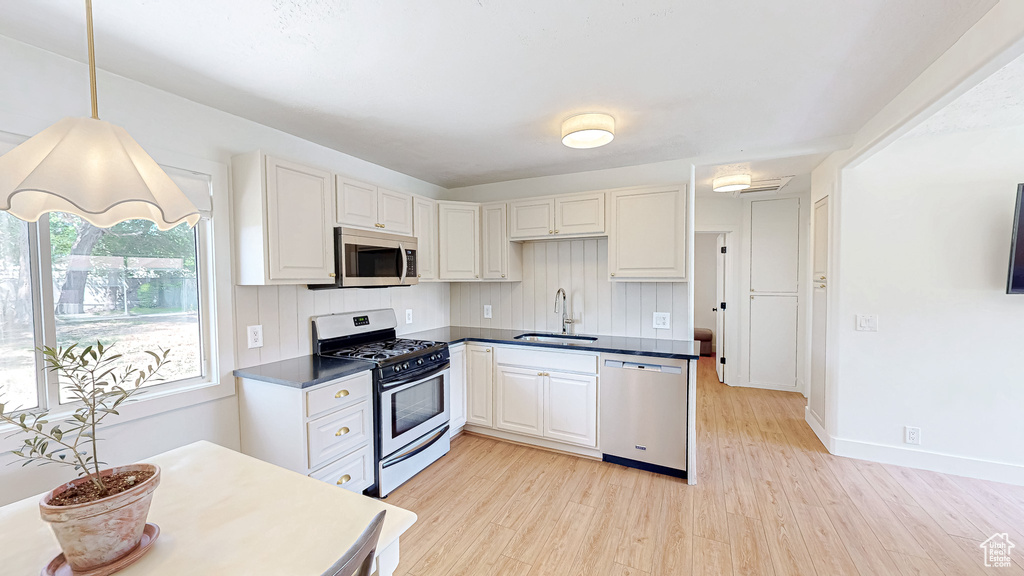 Kitchen featuring stainless steel appliances, a sink, light wood finished floors, and dark countertops