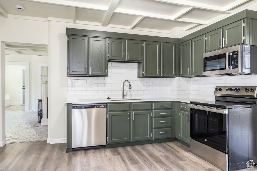 Kitchen with appliances with stainless steel finishes, a sink, light countertops, light wood-style flooring, and coffered ceiling