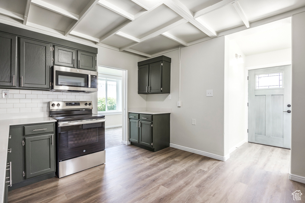 Kitchen featuring appliances with stainless steel finishes, plenty of natural light, light wood-type flooring, backsplash, and beam ceiling
