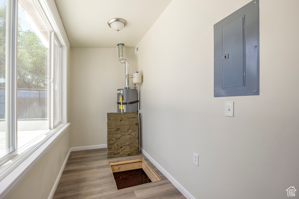 Corridor with electric panel, wood finished floors, baseboards, and water heater