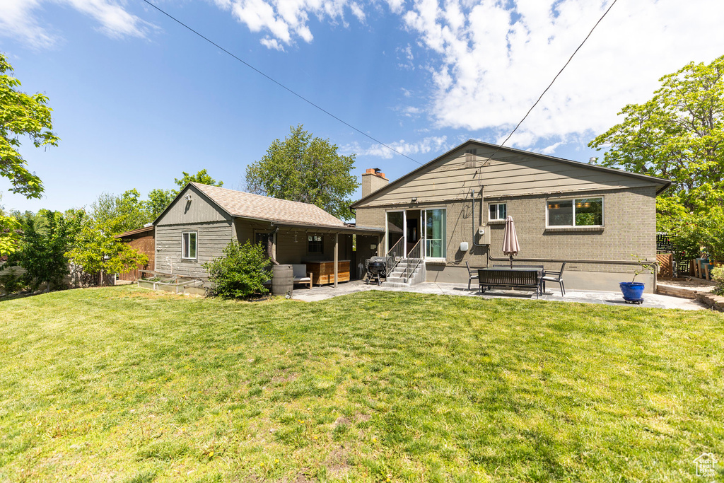 Back of property with a patio, a lawn, entry steps, a chimney, and brick siding