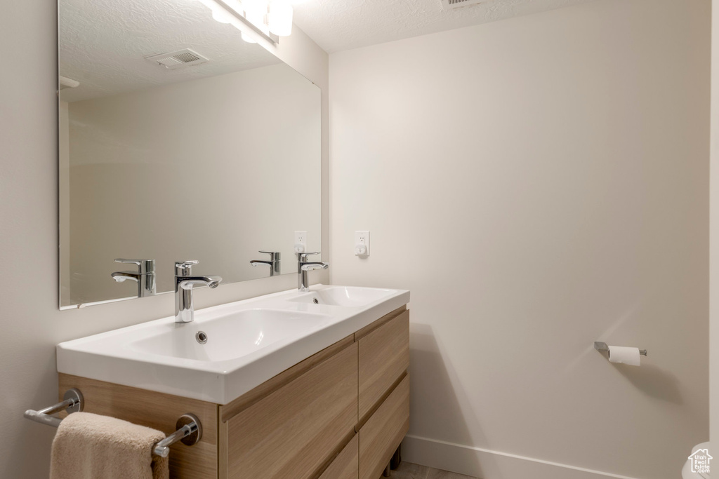 Bathroom featuring double vanity, a textured ceiling, and baseboards