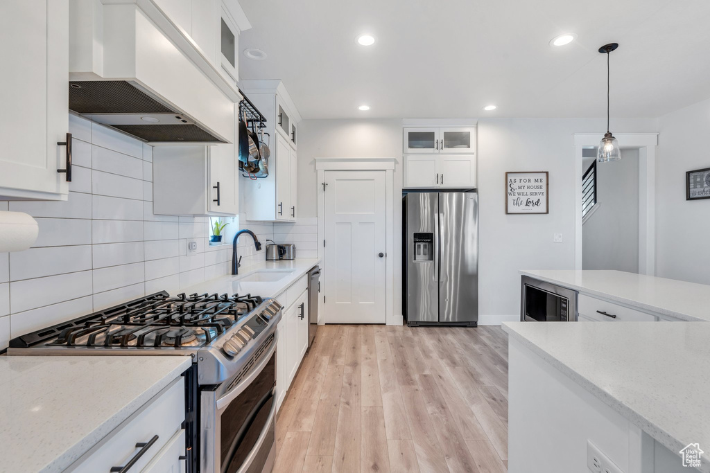 Kitchen featuring appliances with stainless steel finishes, premium range hood, a sink, tasteful backsplash, and light wood-type flooring