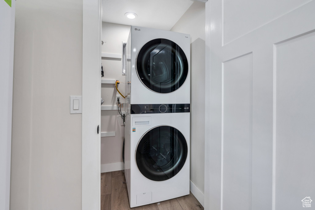 Laundry room featuring stacked washing machine and dryer, wood finished floors, and baseboards