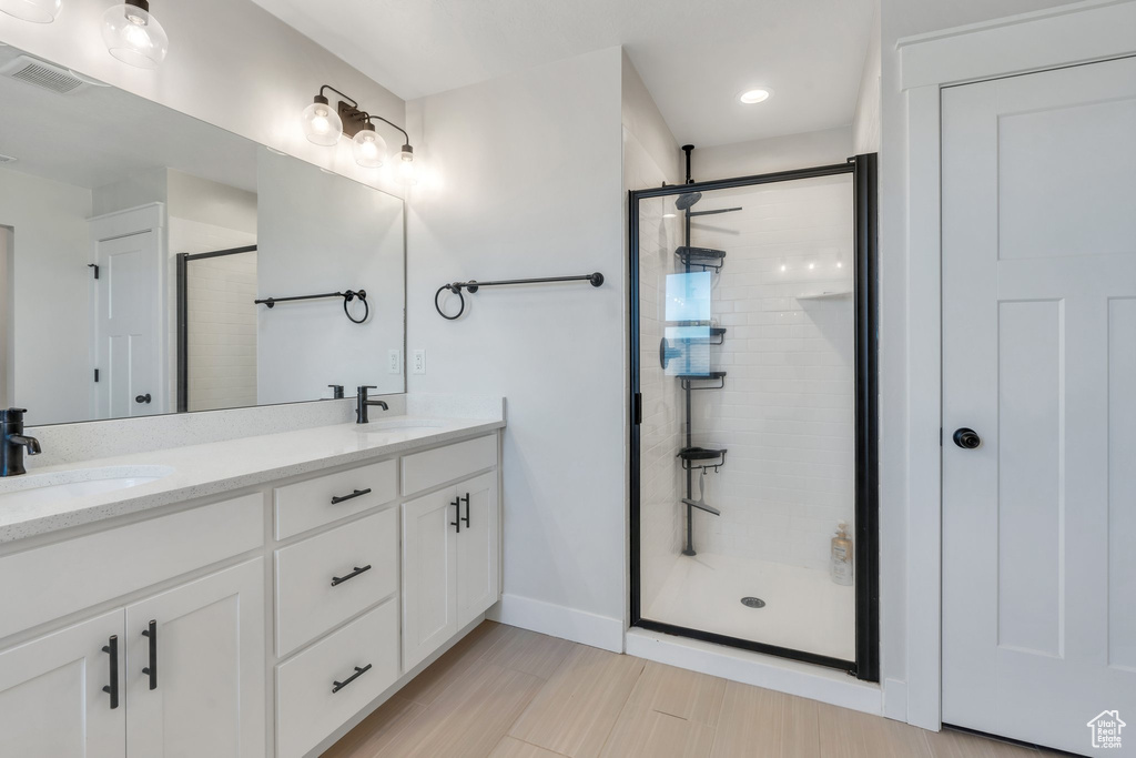 Bathroom featuring a stall shower, double vanity, baseboards, and recessed lighting