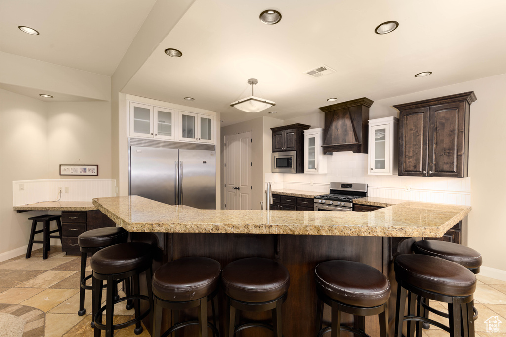 Kitchen with built in appliances, baseboards, dark brown cabinetry, custom exhaust hood, and recessed lighting