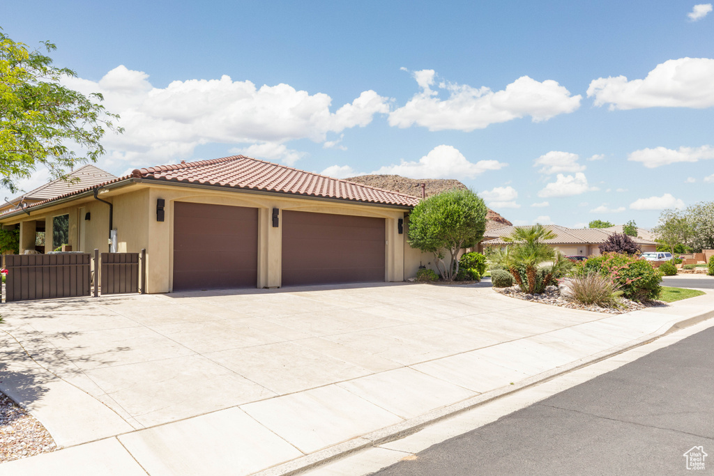 View of front of property with an attached garage, a tiled roof, driveway, and stucco siding