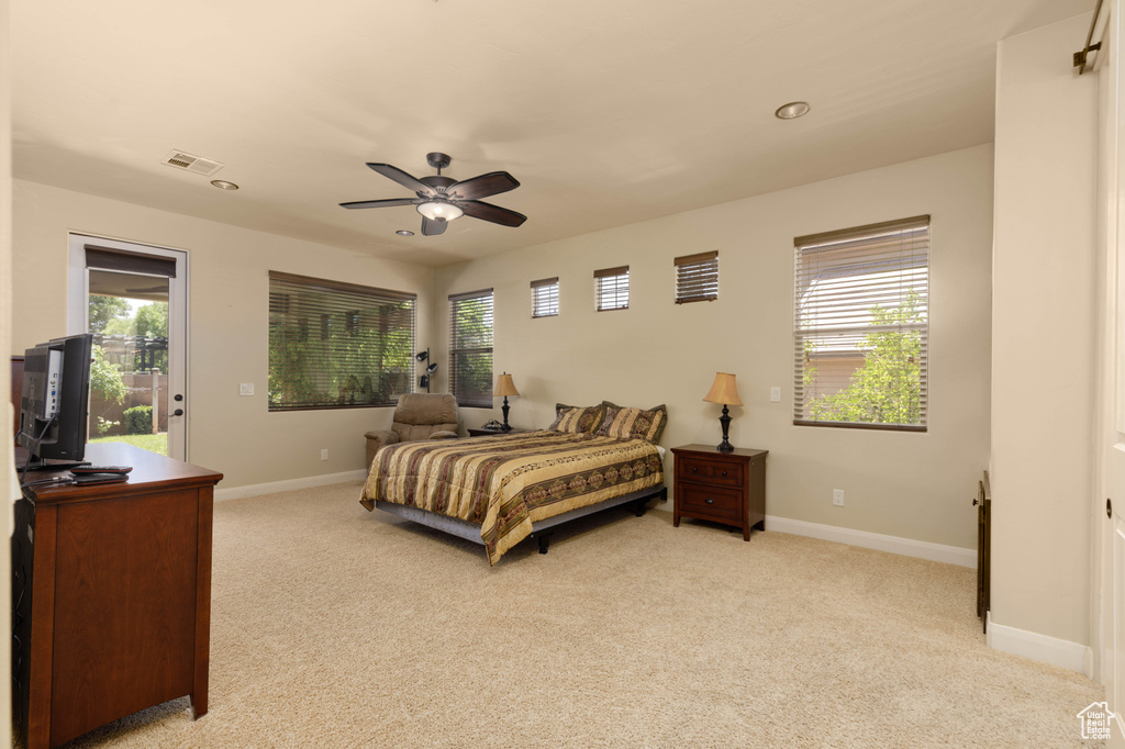 Bedroom with light colored carpet, multiple windows, baseboards, and a ceiling fan