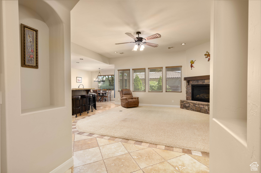 Living area with a bar, a stone fireplace, tile patterned floors, baseboards, and a ceiling fan