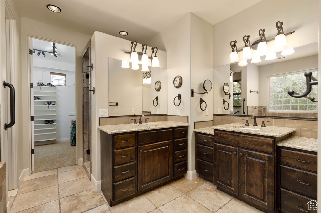 Full bathroom with two vanities, decorative backsplash, and a walk in closet