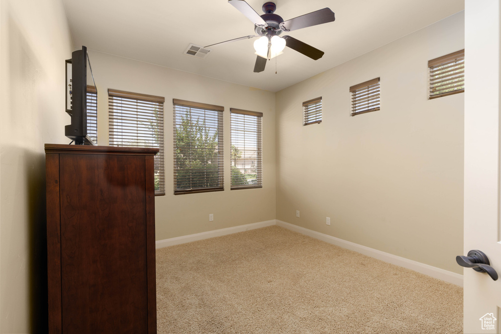 Carpeted empty room featuring healthy amount of natural light, a ceiling fan, and baseboards