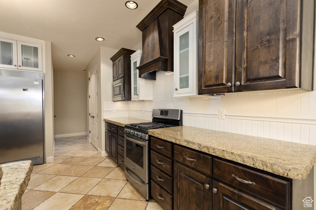Kitchen featuring built in appliances, dark brown cabinetry, decorative backsplash, custom exhaust hood, and recessed lighting